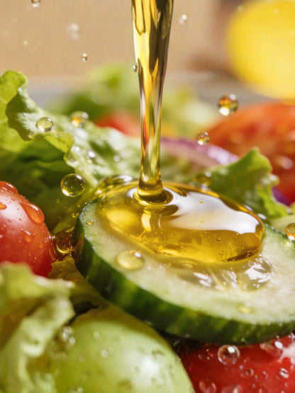 Olive oil being drizzled over a salad with cucumbers, tomatoes, and lettuce.