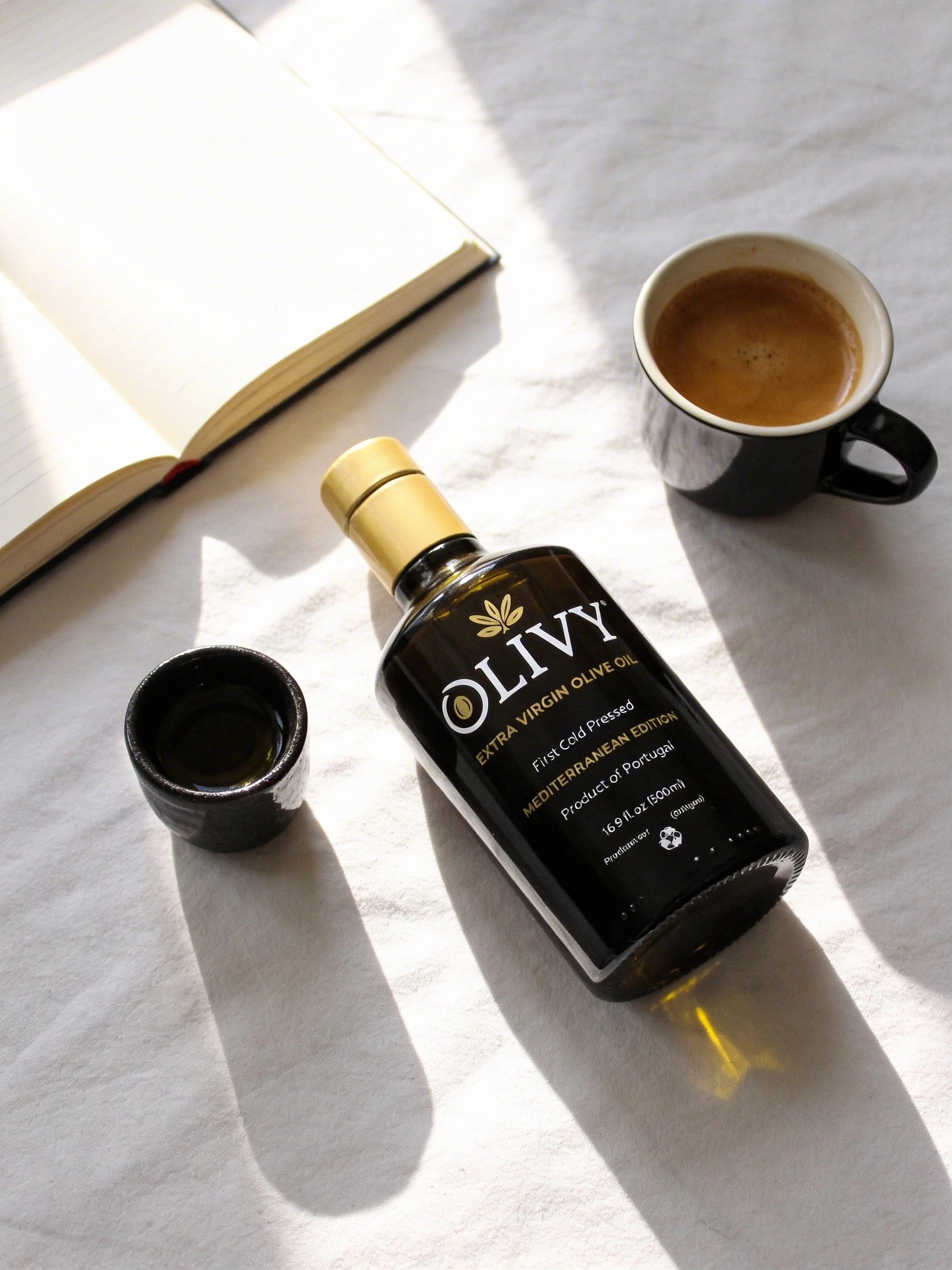Olivy olive oil bottle with a cup of coffee and an open book on a white surface