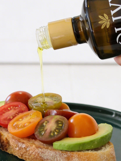 Olive oil being drizzled over sliced tomatoes and avocado on toast