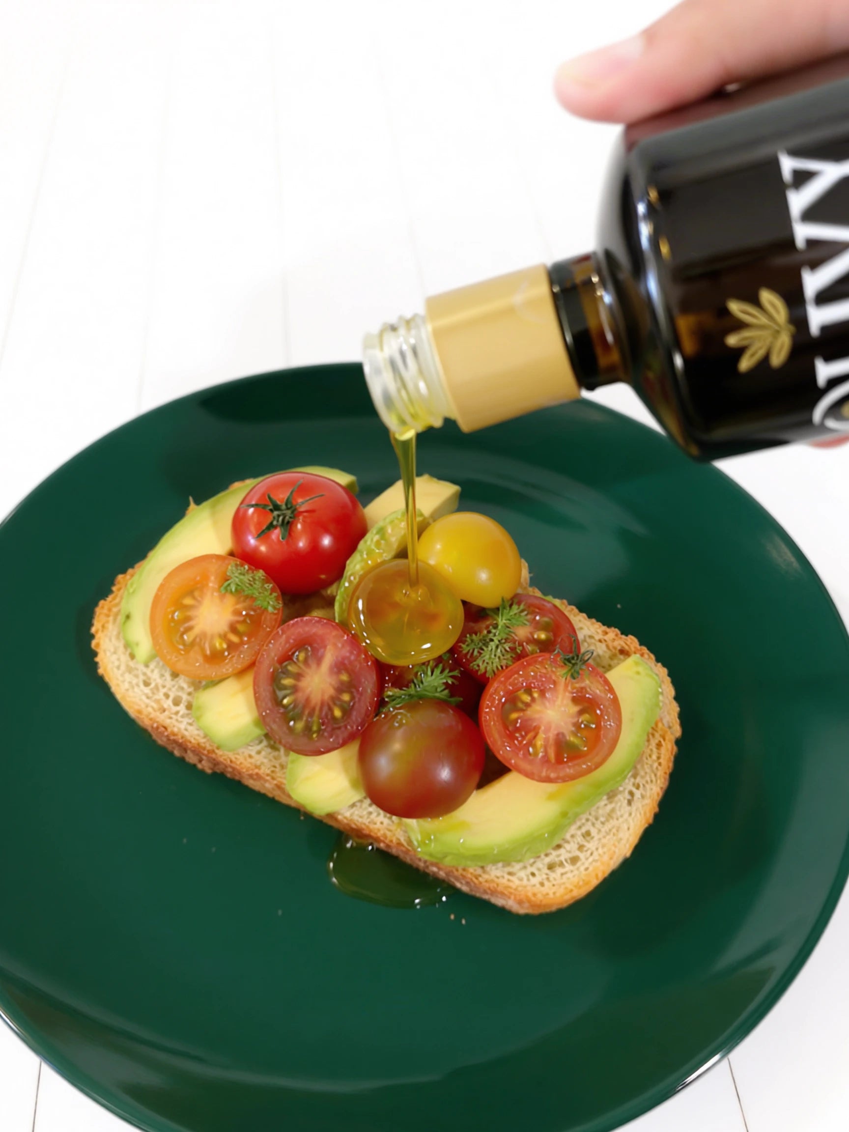 Olive oil being poured onto a avocado toast with tomatoes on a green plate.
