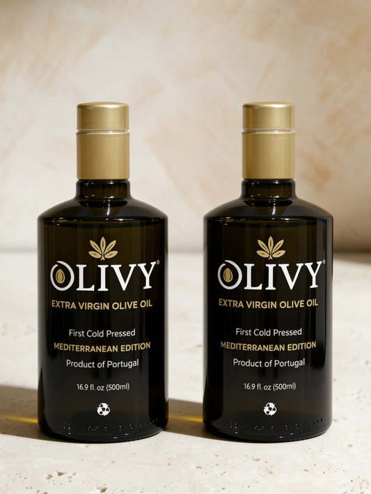 Two dark glass bottles of OLIVY Extra Virgin Olive Oil with gold caps, displayed side-by-side on a light beige textured surface against a matching beige background.