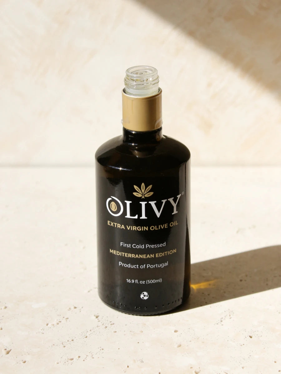 A bottle of OLIVY Extra Virgin Olive Oil, Mediterranean Edition, set on a textured beige stone surface with warm sunlight casting a soft shadow.