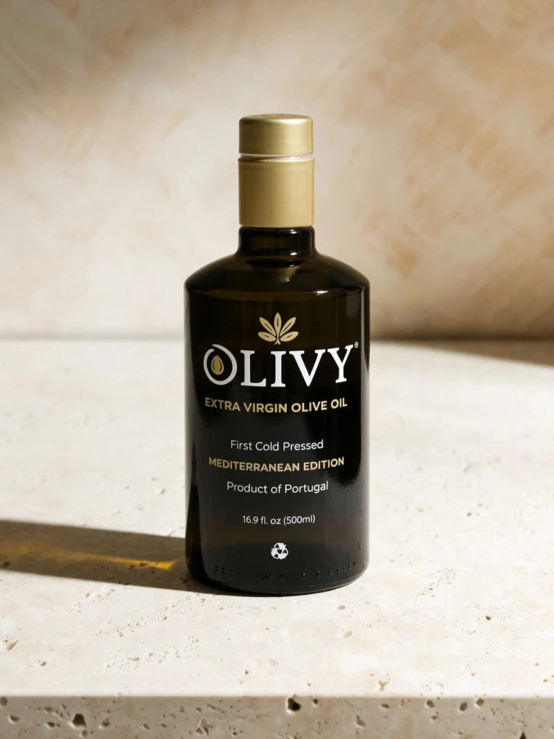 A bottle of OLIVY Extra Virgin Olive Oil, Mediterranean Edition, standing on a textured stone surface with a warm, sunlit beige background.