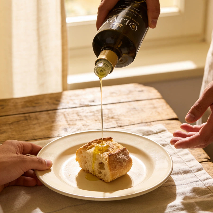 Person pouring olive oil onto bread on a plate with a bottle of olive oil in the background.